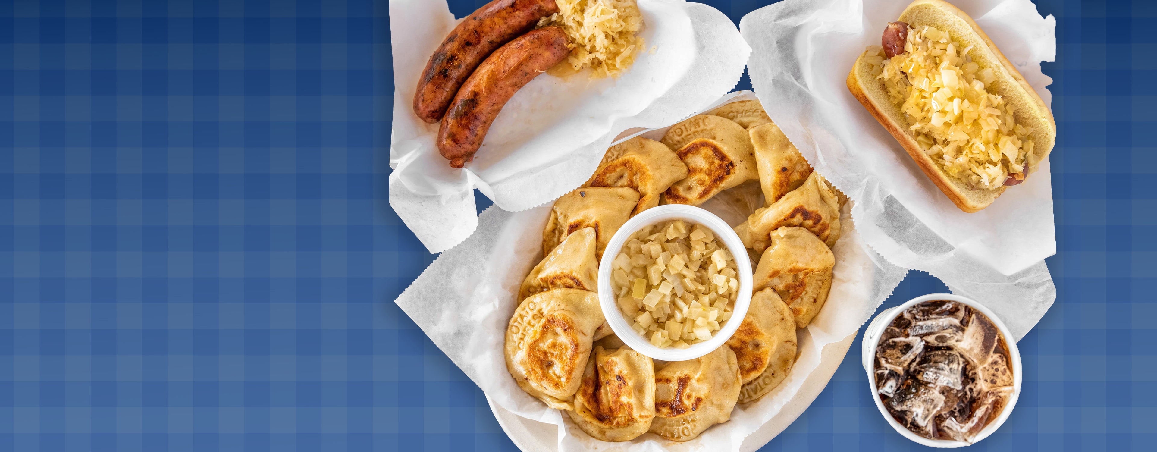 Assorted Pierogi Bros dishes including hot dogs, polish sausages with sauerkraut, pierogis, and drinks on a blue checkered tablecloth background